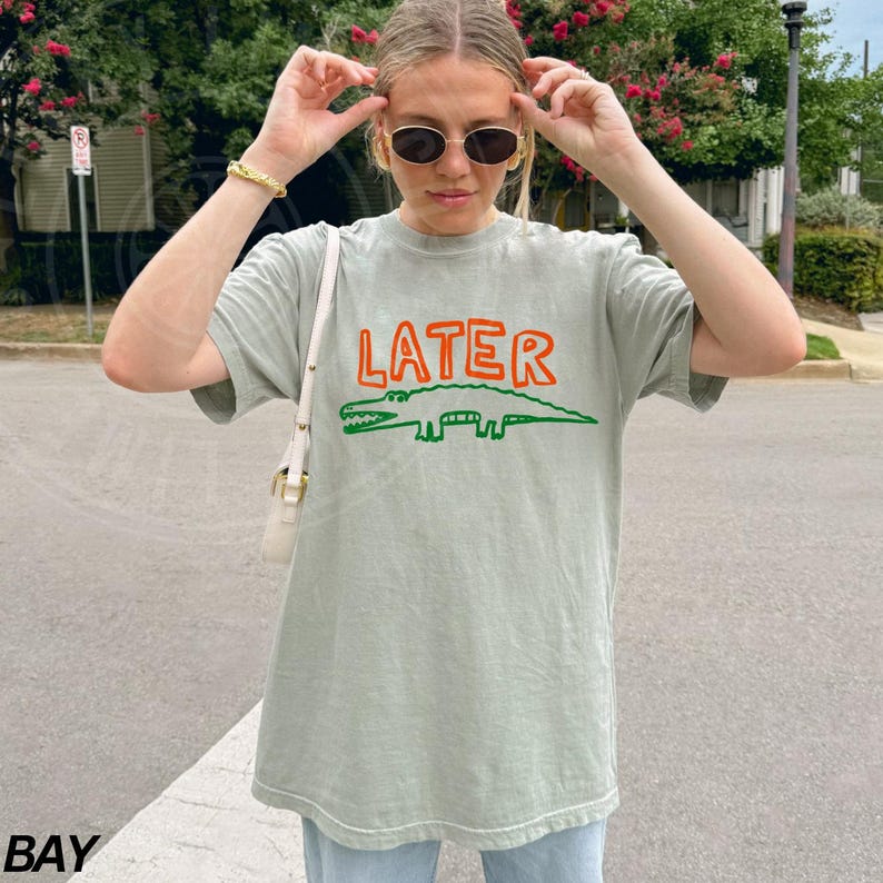 May include: A light green t-shirt with a cartoon alligator and the word "LATER" printed in orange and green.