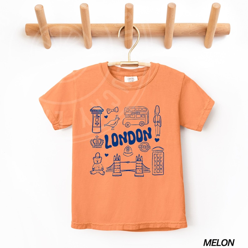 May include: A bright orange t-shirt with a blue graphic of London landmarks, including a double-decker bus, a red telephone box, Big Ben, and the words "LONDON".