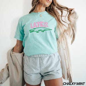 May include: A light blue t-shirt with a green alligator and the word "LATER" in pink letters.