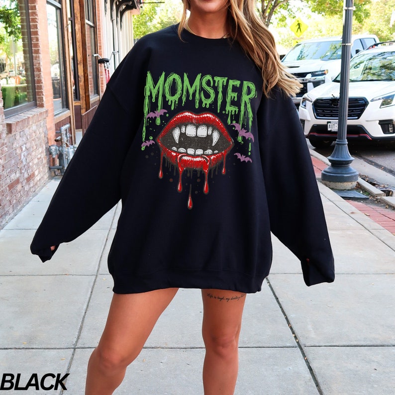 May include: Black sweatshirt with a graphic print of a vampire mouth with fangs and dripping blood. The text "MOMSTER" is printed above the mouth in green.
