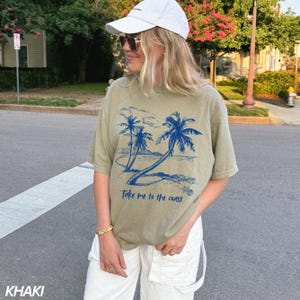 May include: A khaki green t-shirt with a blue graphic of palm trees and the text "Take me to the coast".