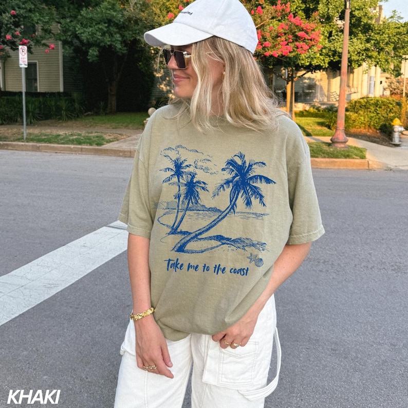 May include: A khaki green t-shirt with a blue graphic of palm trees and the text "Take me to the coast".