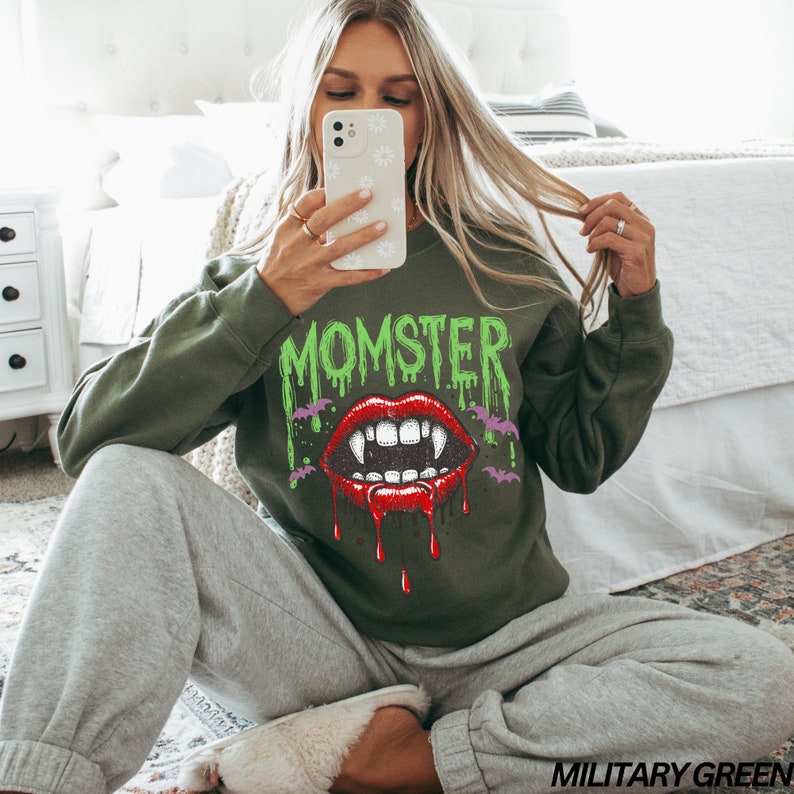 May include: Green sweatshirt with a dripping green "Momster" text and a red vampire mouth with fangs. The mouth is dripping red blood. There are bats around the mouth.