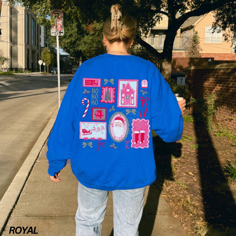 May include: Royal blue sweatshirt featuring a festive Christmas design on the back. The design includes images of Santa Claus, a pink house, candy canes, and the text "HO HO HO". The word "ROYAL" is printed in the bottom left corner.