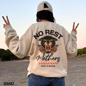 May include: A beige sweatshirt with a black panther graphic and the text "No Rest For The Mothers Born To Endure".