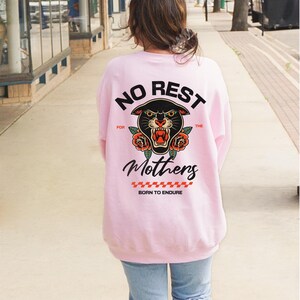May include: A light pink sweatshirt with a black panther graphic and the text "NO REST FOR THE MOTHERS BORN TO ENDURE".