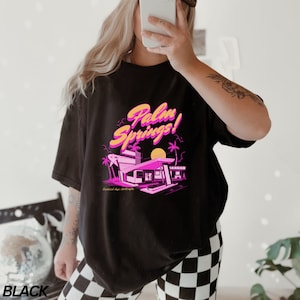 May include: Black oversized t-shirt featuring a pink and yellow graphic print of a retro motel with the text "Palm Springs!" and the words "Sunsoaked days, desert nights".