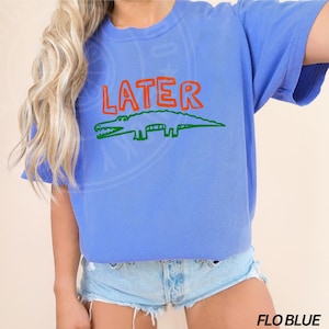 May include: A blue t-shirt with the word "LATER" in orange and a green alligator graphic.