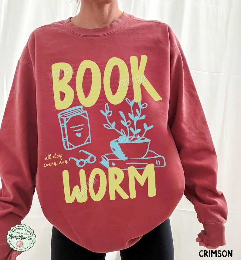 May include: Crimson-colored sweatshirt with a yellow "BOOK WORM" graphic. The design includes a book, glasses, and a potted plant. The text "all day every day" is also included in the design.
