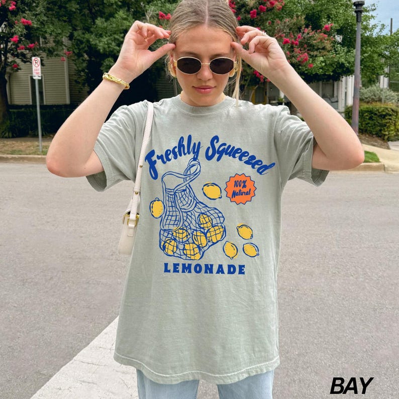 Puede incluir: Una camiseta verde claro con un gr&aacute;fico de una bolsa de limones y el texto "Freshly Squeezed 100% Natural LEMONADE".