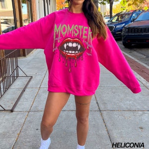 May include: A pink sweatshirt with a graphic print of a dripping vampire mouth with fangs and the word "MOMSTER" above it.