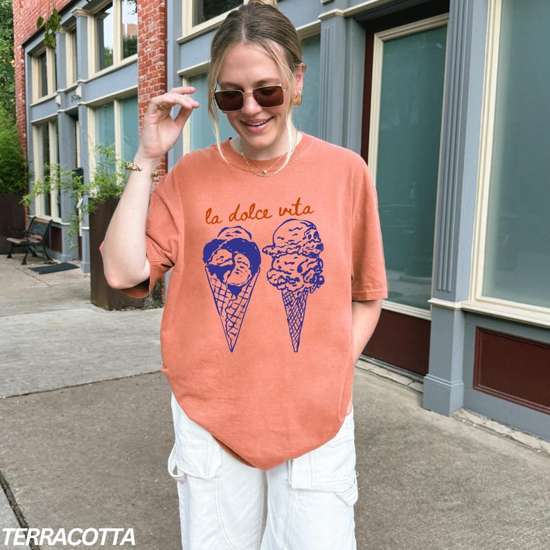 May include: A terracotta orange t-shirt with a graphic of two ice cream cones. The text "la dolce vita" is printed above the ice cream cones.