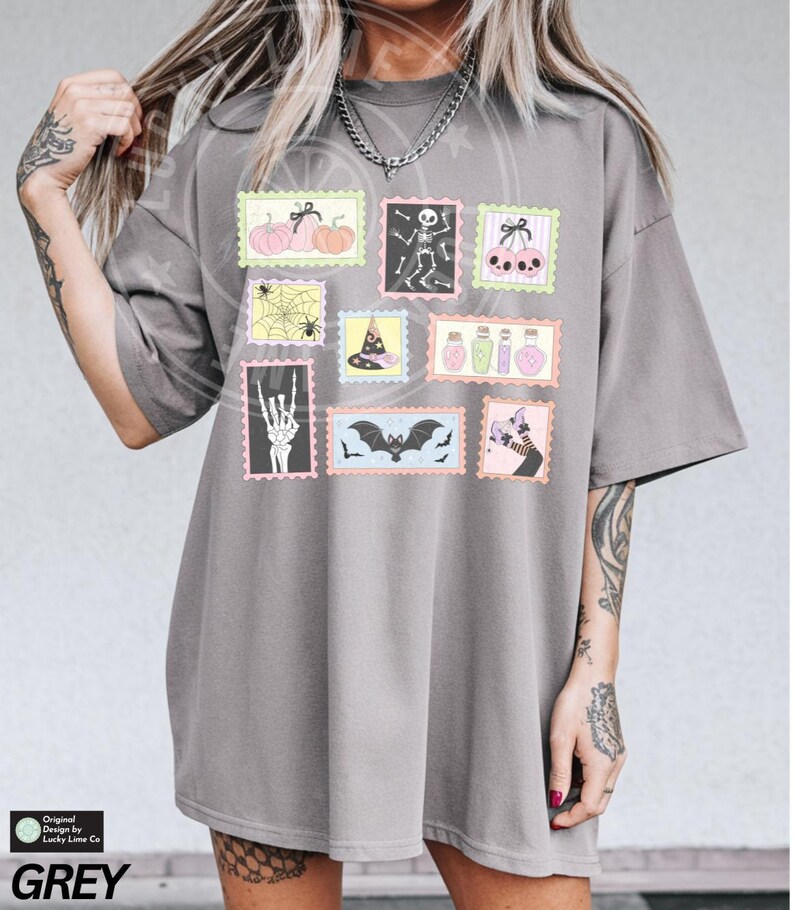 May include: Grey t-shirt featuring Halloween-themed postage stamp designs. The stamps depict pumpkins, skeletons, bats, witch hats, potion bottles, and a skeleton hand. The text "GREY" is at the bottom of the shirt.