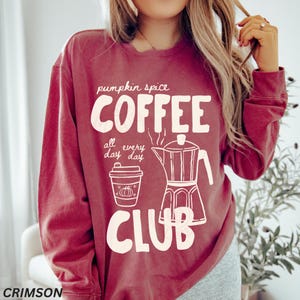 May include: Crimson-colored sweatshirt with the words "Pumpkin Spice Coffee Club" in white, along with a coffee cup and a coffee maker illustration. The text "all every day day" is also included.