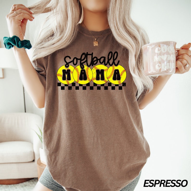 Op de afbeelding: Bruin T-shirt met de tekst "Softball Mama" in zwarte letters. Vier gele softball-afbeeldingen zijn rond de tekst gerangschikt.
