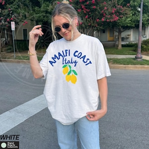 K&ouml;nnte beinhalten: Wei&szlig;es T-Shirt mit einer blauen Grafik, auf der "Amalfi Coast Italy" mit einer Gruppe gelber Zitronen steht.