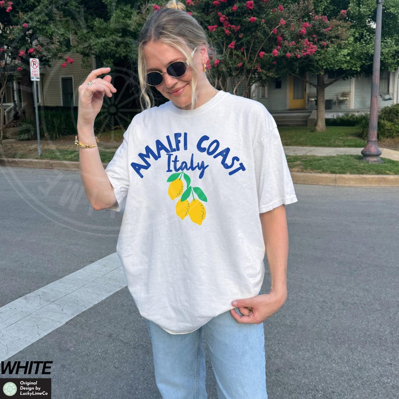 K&ouml;nnte beinhalten: Wei&szlig;es T-Shirt mit einer blauen Grafik, auf der "Amalfi Coast Italy" mit einer Gruppe gelber Zitronen steht.