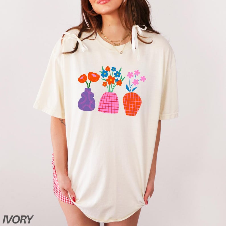 May include: A white t-shirt with a graphic of three vases with colorful flowers. The vases are purple, pink and orange.