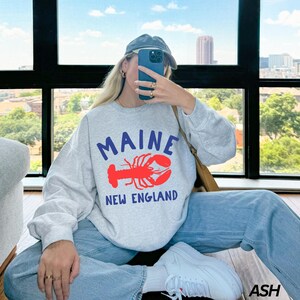 May include: A gray sweatshirt with a red lobster graphic and the text "Maine New England".