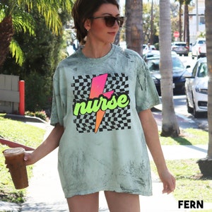 May include: A light green t-shirt with a black and white chequered pattern and a pink and green lightning bolt graphic. The text "nurse" is written in a stylised font on the graphic.