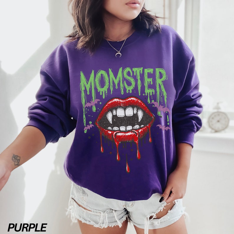 May include: Purple sweatshirt with a graphic print of a dripping green "Momster" text and a red vampire mouth with fangs.