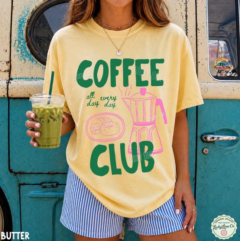 Peut inclure: Un t-shirt jaune p&acirc;le &agrave; manches courtes avec le texte vert COFFEE CLUB et un contour rose d'une cafeti&egrave;re italienne avec une p&acirc;tisserie. Le t-shirt porte le texte all every day en petites lettres vertes. Un gobelet en plastique de th&eacute; glac&eacute; vert.