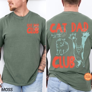 Peut inclure: T-shirt vert mousse avec l'inscription "CAT DAD CLUB" en rouge &agrave; l'avant et &agrave; l'arri&egrave;re. Le dos pr&eacute;sente &eacute;galement des illustrations de chats et l'expression "life is better with cats" en turquoise. Un tee-shirt d&eacute;contract&eacute; et confortable.