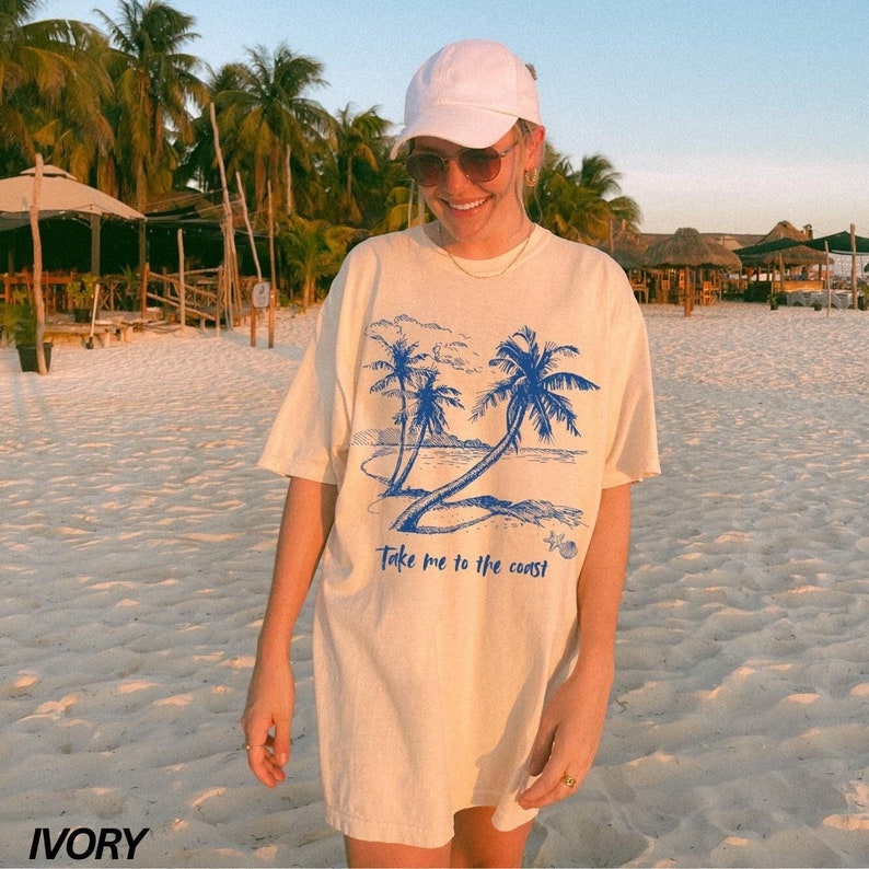 May include: A cream colored t-shirt with a blue graphic of palm trees and the text "Take me to the coast".