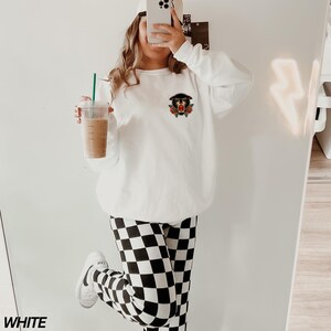 May include: White sweatshirt with a black panther graphic and red roses. The sweatshirt is paired with black and white checkered leggings.