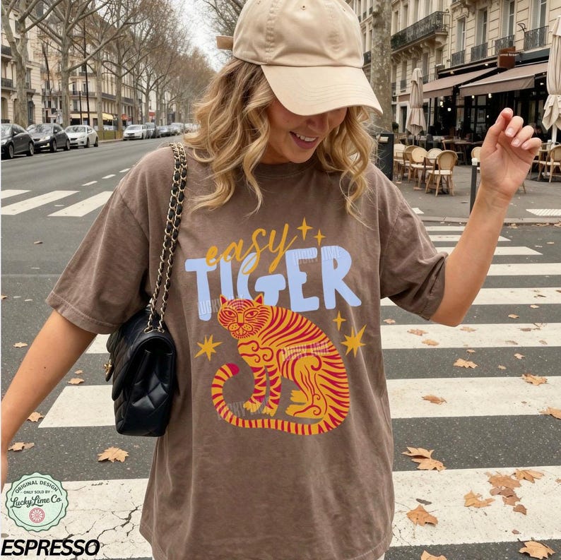 May include: Brown t-shirt with the text "easy TIGER" in blue and yellow, featuring a tiger illustration in red and yellow. The shirt is part of the "Lucky Lime Co" original design collection.