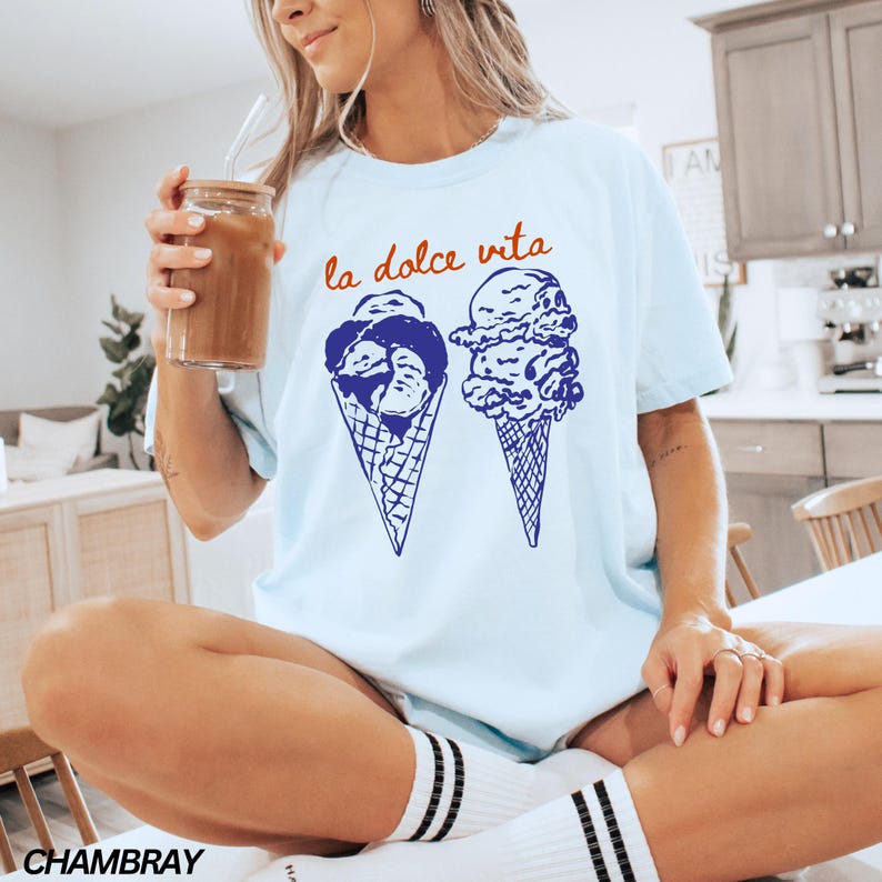 May include: A light blue t-shirt with the text "la dolce vita" in orange and blue. The shirt features a graphic of two ice cream cones with blue and white swirls.