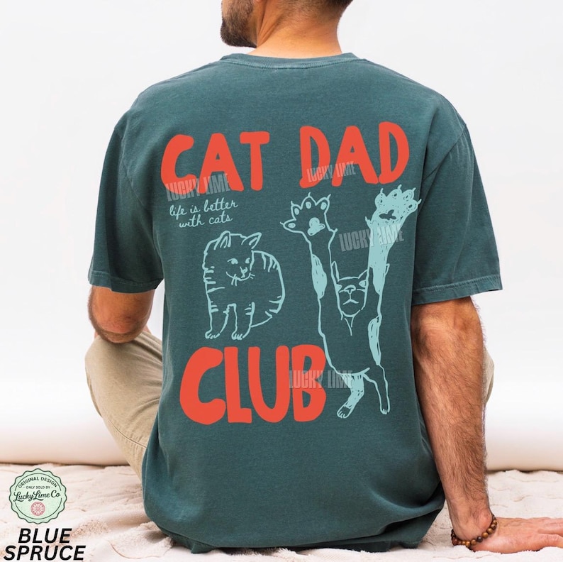Peut inclure: T-shirt bleu sarcelle avec l'inscription "CAT DAD CLUB" en lettres rouges. Le t-shirt pr&eacute;sente un motif de chat et la phrase "life is better with cats" en blanc. C'est un design Blue Spruce.