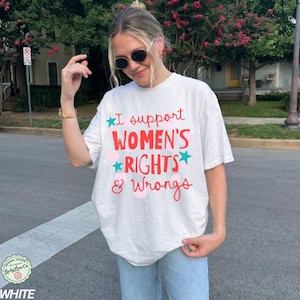 Peut inclure: T-shirt blanc avec l'inscription "I support WOMEN'S RIGHTS & Wrongs" en rouge, bleu et rose. Le t-shirt a une coupe ample et des manches courtes. Le motif comprend des &eacute;toiles et des cercles.