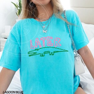 May include: A turquoise blue t-shirt with a green alligator and the word "LATER" in pink lettering.