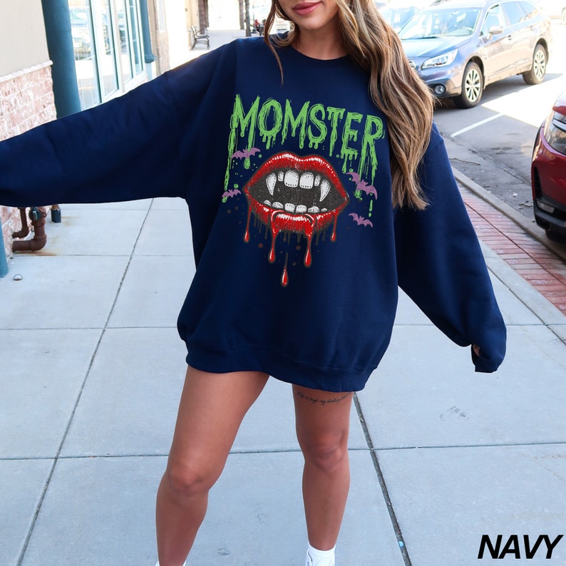May include: A navy blue sweatshirt with the text "MOMSTER" in green letters and a graphic of a red vampire mouth with dripping blood.