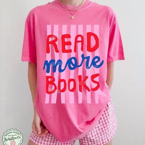 Puede incluir: Una camiseta rosa con las palabras "READ more BOOKS" en rojo y azul, sobre un fondo de rayas rosas. Se combina con pantalones cortos a cuadros rosas y blancos. El dise&ntilde;o incluye un logotipo que dice "Lucky Lime Co" y la palabra "CRUNCHBERRY".