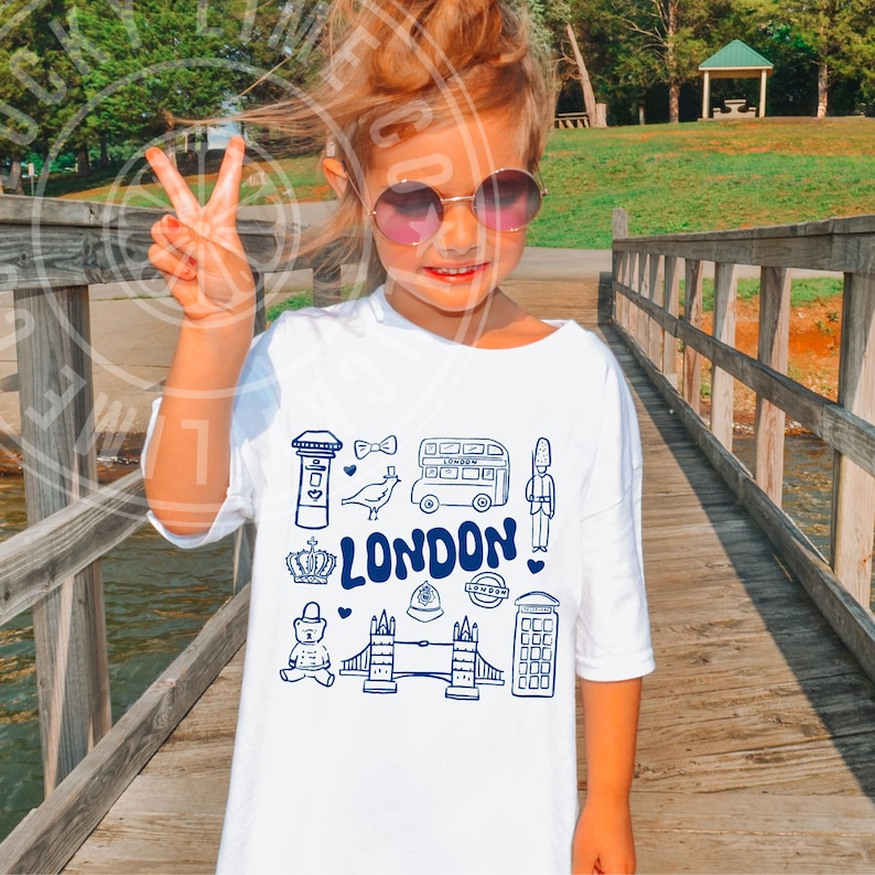 May include: A white t-shirt featuring a blue graphic of London landmarks, including a double-decker bus, Big Ben, a red telephone box, and the words "LONDON".