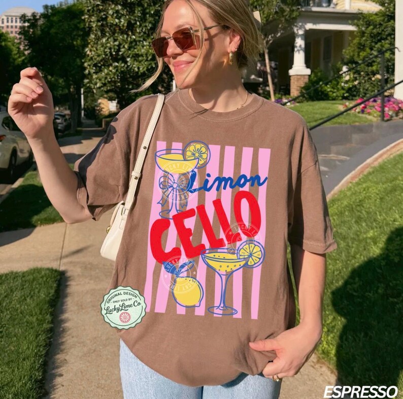 May include: Espresso-colored t-shirt with a graphic design featuring the words "Limon Cello" in blue and red, along with illustrations of cocktails and lemons. The shirt has a relaxed fit and short sleeves.
