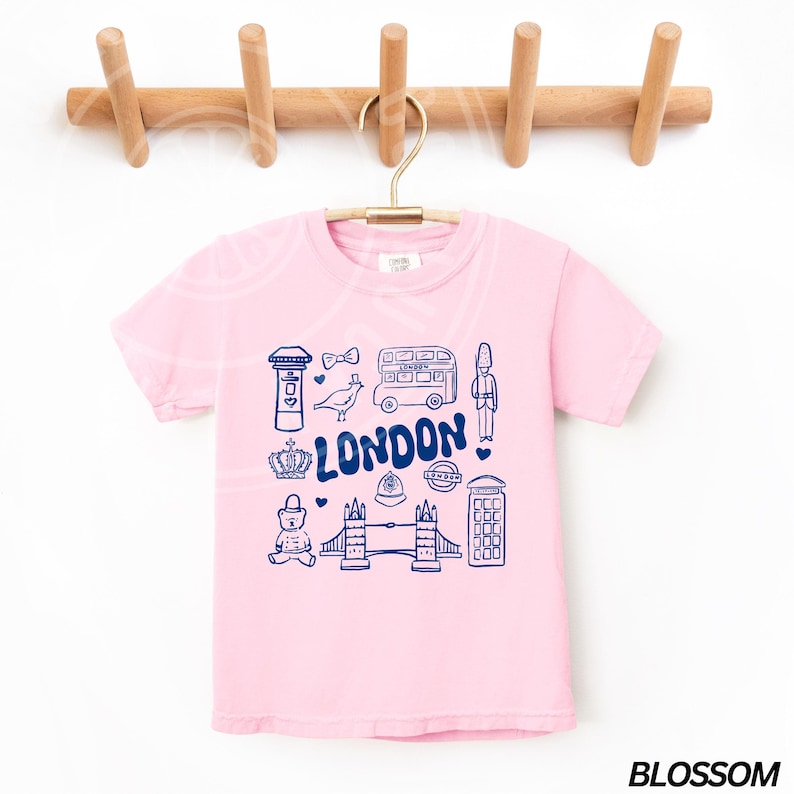 May include: Pink short-sleeved t-shirt with a blue graphic of London landmarks, including a double-decker bus, a red telephone box, Big Ben, and the words "LONDON".
