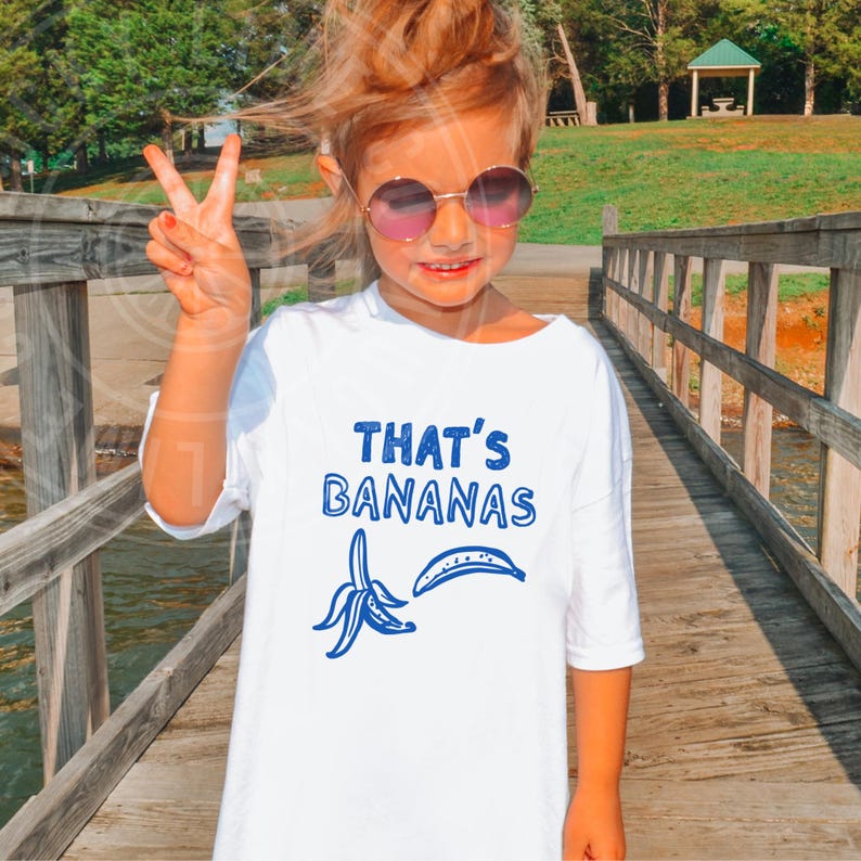 Op de afbeelding: Wit T-shirt met blauwe tekst die "That's Bananas" zegt en een blauwe illustratie van twee bananen.