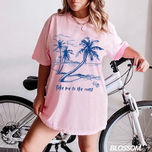 May include: Pink t-shirt with a blue graphic of palm trees on a beach and the text "Take me to the coast".