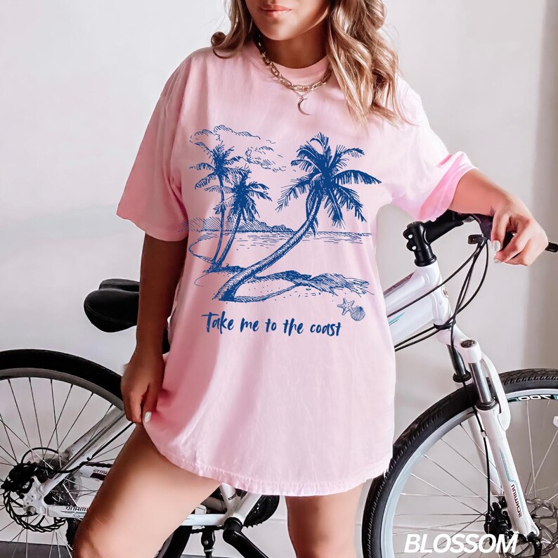 May include: Pink t-shirt with a blue graphic of palm trees on a beach and the text "Take me to the coast".