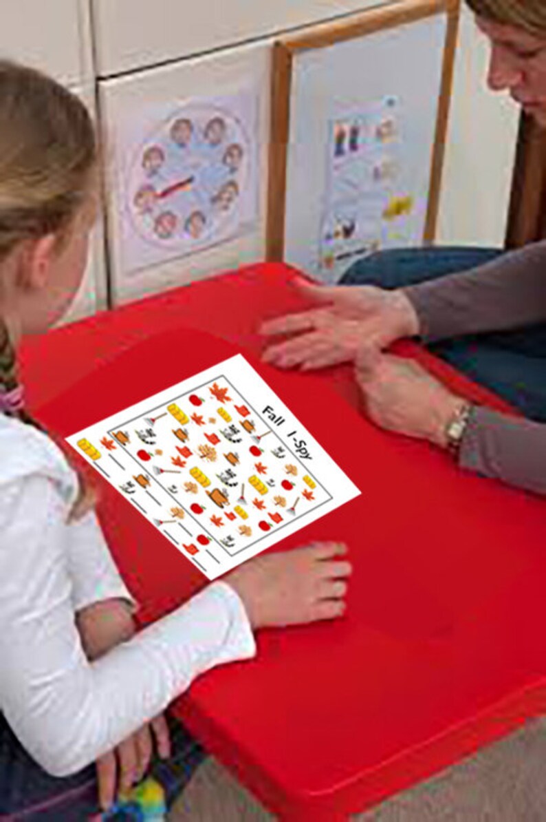 May include: A white sheet of paper with a fall-themed I Spy game. The paper has a red border and is filled with small images of fall leaves, pumpkins, apples, and other fall-related items. The text "Fall I-Spy" is printed in black at the top of the paper.