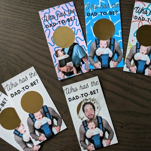 May include: Five white cards with gold circles and the text "Who has the DAD-TO-BE?" printed on them. Each card features a different photo of a person holding a baby in a baby carrier.