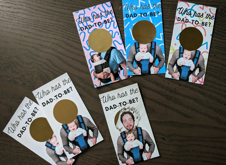 May include: Five white cards with gold circles and the text "Who has the DAD-TO-BE?" printed on them. Each card features a different photo of a person holding a baby in a baby carrier.