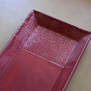 May include: A rectangular, red ceramic serving tray. The tray features a floral pattern on the rim and a smooth, glossy finish. The tray is ideal for serving appetizers or displaying decorative items. The tray's dimensions are approximately 12 inches long and 6 inches wide.