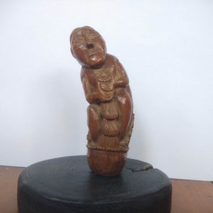 Può includere: Una scultura in legno di una persona con un viso dettagliato e intagli intricati sul corpo. La scultura è di colore marrone e ha una base arrotondata.