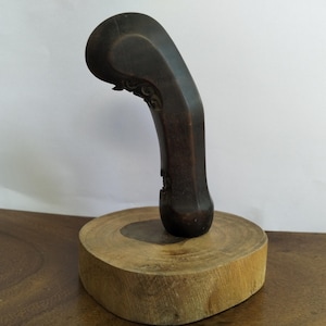 May include: A dark brown wooden handle with intricate carvings, displayed on a wooden base. The handle is shaped like a curved, stylized bird's head.