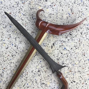 May include: A traditional Indonesian keris, a double-edged dagger with a wavy blade, is crossed over a wooden scabbard with a curved handle. The keris is a symbol of power and authority in Indonesian culture.
