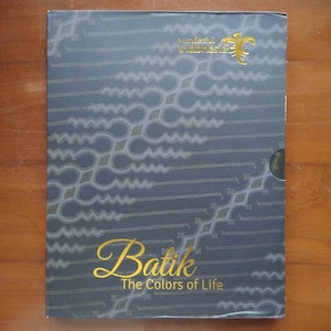 Può includere: Una copertina di libro con sfondo blu e un motivo dorato. Il titolo "Batik: The Colors of Life" è scritto in lettere dorate. La copertina del libro presenta anche un logo dorato con il testo "Wonderful Indonesia".